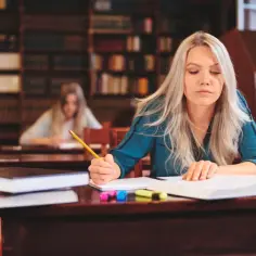 Kobieta uczy się w bibliotece, zastanawiając się, ile kosztuje poprawa egzaminu zawodowego.