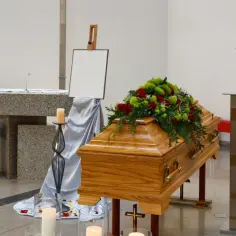 Drewniana trumna z kwiatami, świece i krzyż. Zastanawiasz się, ile zarabia się w domu pogrzebowym?