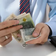 Mężczyzna w koszuli i krawacie liczy polskie banknoty. Zastanawia się, ile pracodawca płaci za pracownika na pół etatu.