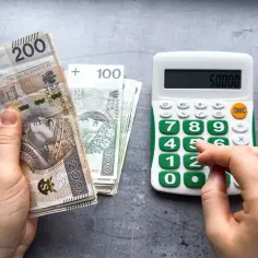 Ręka liczy pieniądze, by sprawdzić, czy wystarczą na pokrycie płacy minimalnej brutto. Kalkulator pokazuje 50000.