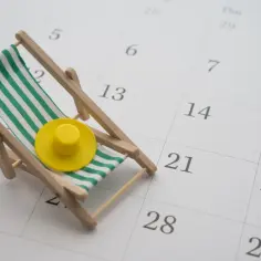 Mini leżak z żółtym kapeluszem na kalendarzu. Czas zaplanować, ile dni urlopu wypoczynkowego potrzebujesz na relaks.