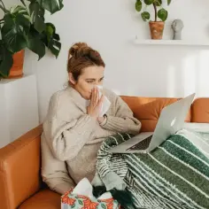 Kobieta na chorobowym z laptopem i chusteczkami, szuka informacji czy na chorobowym płaci się ZUS.