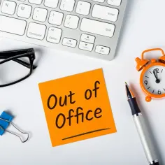 Biurko z notatką "Out of Office", okularami, długopisem i budzikiem. Pracownik ma wolne, zastanawia się, ile urlopu ma pracownik.