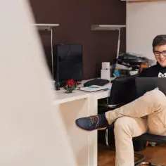 Uśmiechnięty mężczyzna na stażu pracuje przy laptopie. Czy po zakończeniu stażu pracodawca musi zatrudnić?