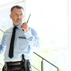 Ochroniarz z pozwoleniem na broń, w jasnej koszuli i czarnym krawacie, trzyma krótkofalówkę. Zastanawiasz się, ile zarabia ochroniarz z pozwoleniem na broń?