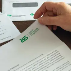 Dłoń przegląda dokumenty z ZUS, pokazując, jak sprawdzić przepracowane lata i informacje o stanie konta ubezpieczonego.
