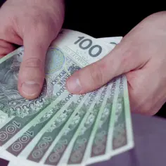 Dłonie trzymają stos banknotów po 100 zł. Zastanawiasz się, ile wynosi pensja na pół etatu?