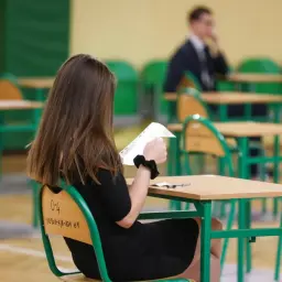 Dziewczyna w czarnej sukience trzyma kartkę, czekając na wyniki egzaminów zawodowych.