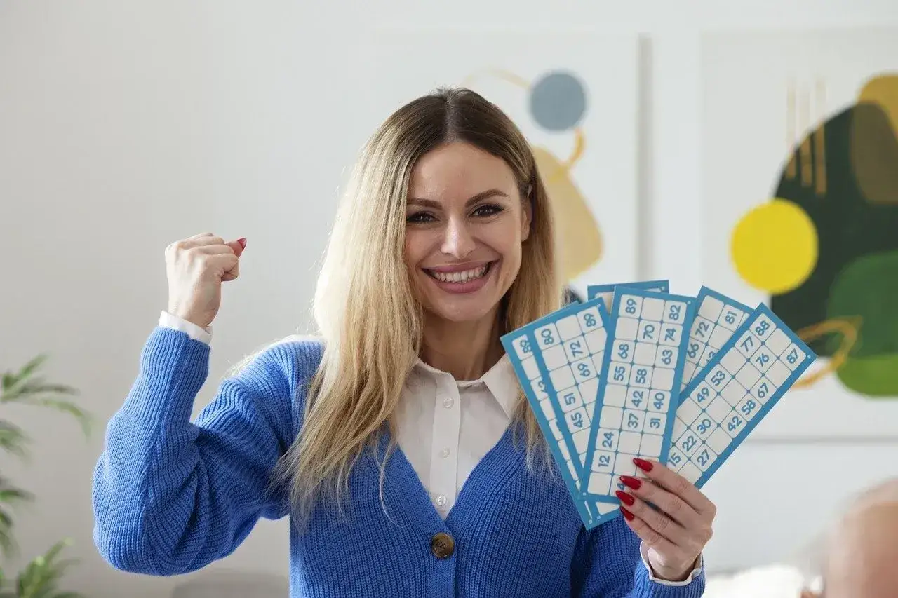 Uśmiechnięta kobieta z kartami do gry w bingo, zaciśnięta pięść w geście triumfu. Czy to dlatego pracownicy nie mogą brać udziału w loteriach organizowanych przez firmę?