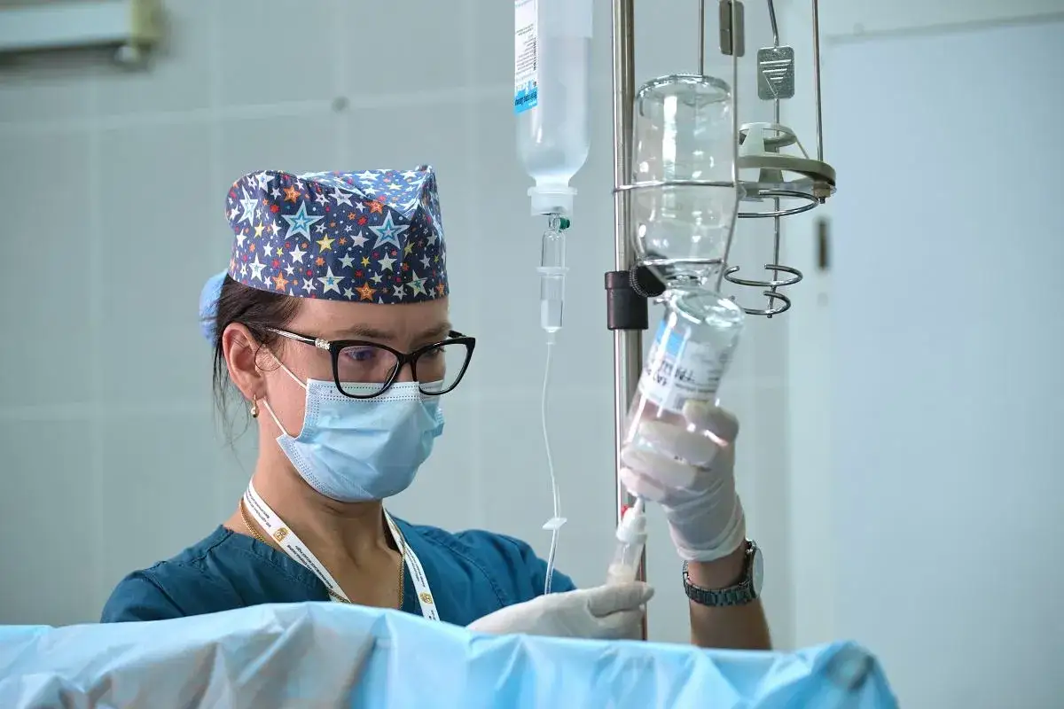 Pielęgniarka w maseczce i czepku z gwiazdkami przygotowuje kroplówkę. Ile zarabia pielęgniarka w szpitalu? To pytanie nurtuje wiele osób.