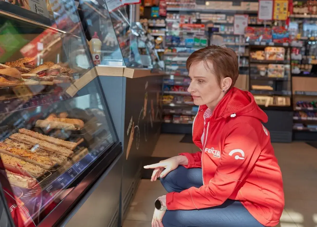 Kierowniczka stacji ORLEN sprawdza ofertę. Ciekawe, ile zarabia kierownik stacji ORLEN, dbając o świeżość przekąsek.