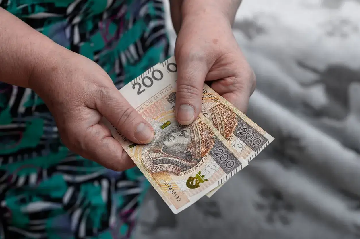 Dłonie trzymają dwie dwustuzłotowe banknoty. Czy to wystarczy, by sprawdzić przepracowane lata i godnie żyć?