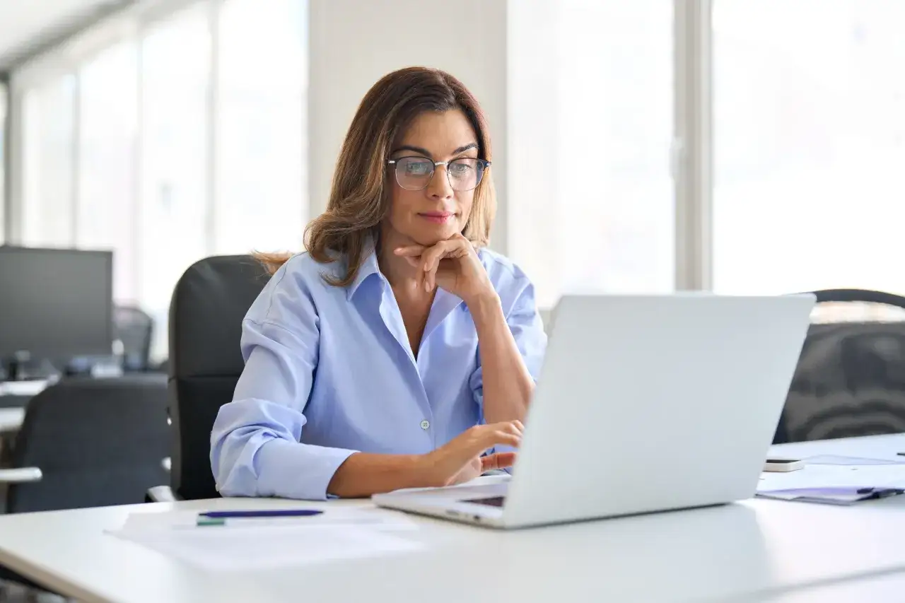 Kobieta w okularach siedzi przy biurku i pracuje na laptopie, zastanawiając się, jak sprawdzić ile ma się lat pracy.