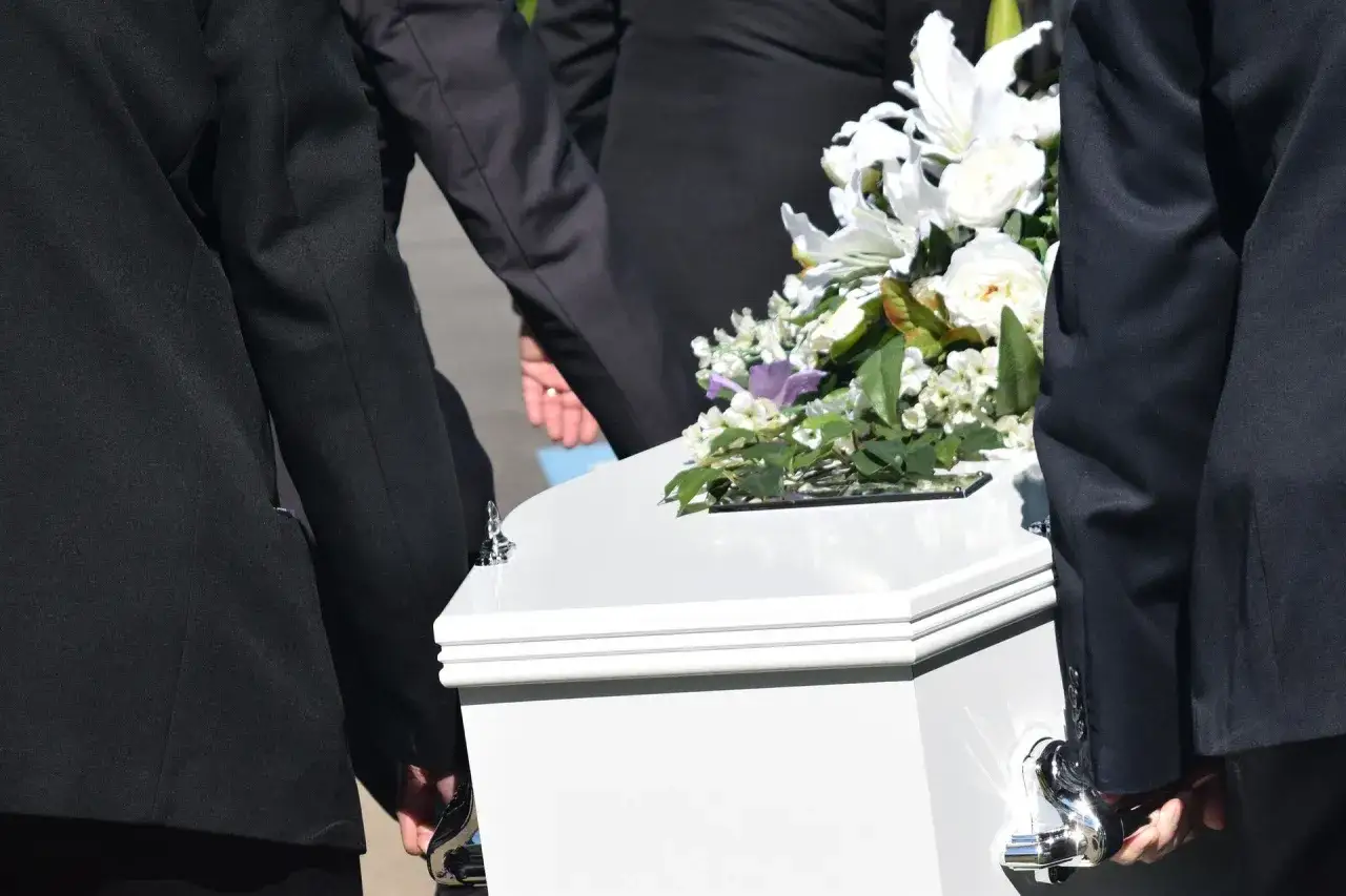 Konduktorzy niosą białą trumnę z kwiatami. Zastanawiasz się, ile się zarabia w zakładzie pogrzebowym?