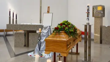 Drewniana trumna z kwiatami, świece i krzyż. Zastanawiasz się, ile zarabia się w domu pogrzebowym?