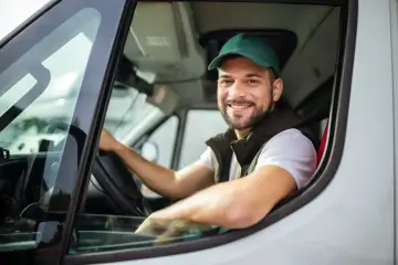 Uśmiechnięty kurier DPD w zielonej czapce siedzi za kierownicą. Zastanawiasz się, ile zarabia kurier DPD?