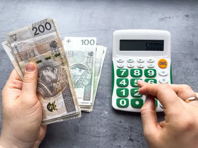 Ręka liczy pieniądze, by sprawdzić, czy wystarczą na pokrycie płacy minimalnej brutto. Kalkulator pokazuje 50000.