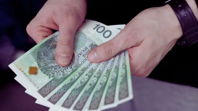 Dłonie trzymające stos banknotów 100-złotowych.